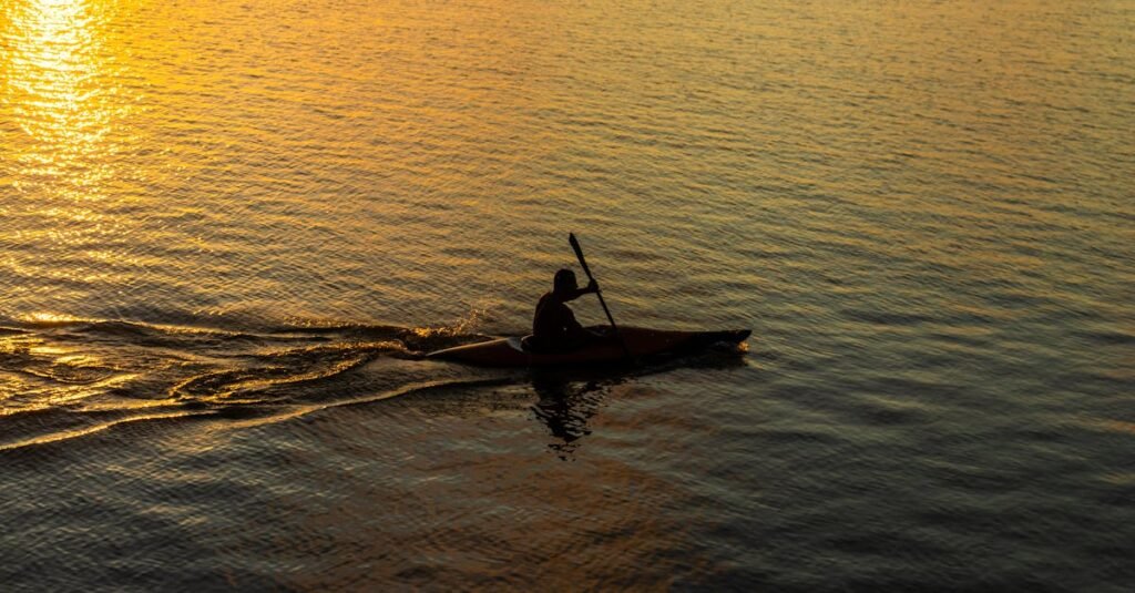 A kayaker paddling in silhouette against a stunning sunset on Brazilian waters, creating a tranquil scene.